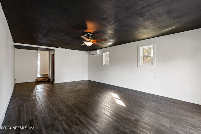 empty room featuring a textured ceiling, a wall mounted AC, dark hardwood / wood-style floors, and ceiling fan