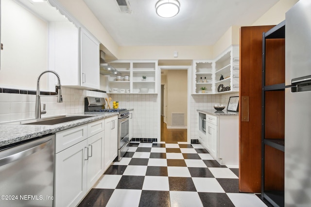 kitchen featuring wall chimney range hood, sink, white cabinets, appliances with stainless steel finishes, and tasteful backsplash