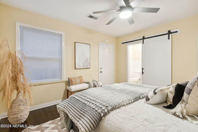 bedroom featuring a barn door, ensuite bath, dark wood-type flooring, and ceiling fan