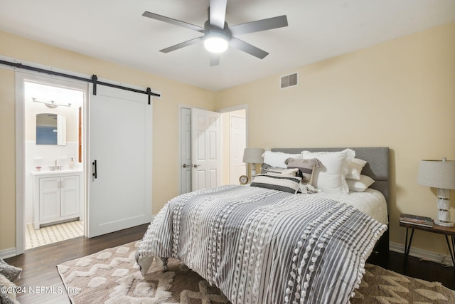 bedroom with ceiling fan, a barn door, connected bathroom, dark hardwood / wood-style floors, and sink