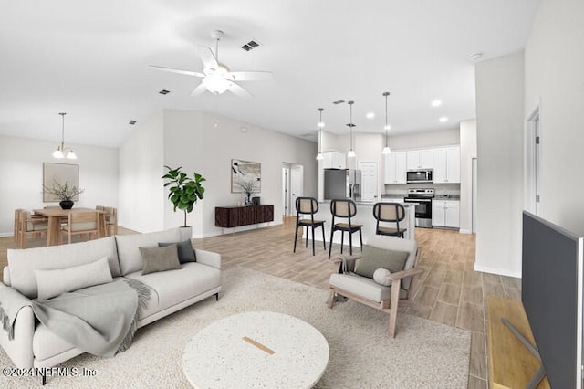 living room with light hardwood / wood-style flooring, vaulted ceiling, and ceiling fan