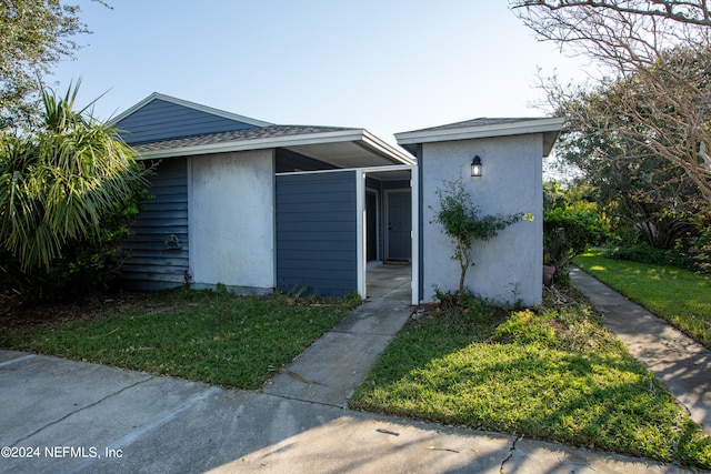 view of front of property featuring stucco siding, roof with shingles, and a front lawn