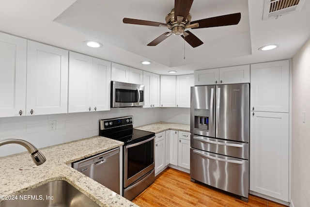 kitchen featuring light wood-type flooring, a sink, white cabinetry, appliances with stainless steel finishes, and a raised ceiling