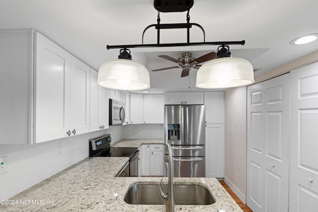 kitchen with light stone countertops, appliances with stainless steel finishes, hanging light fixtures, white cabinets, and a sink