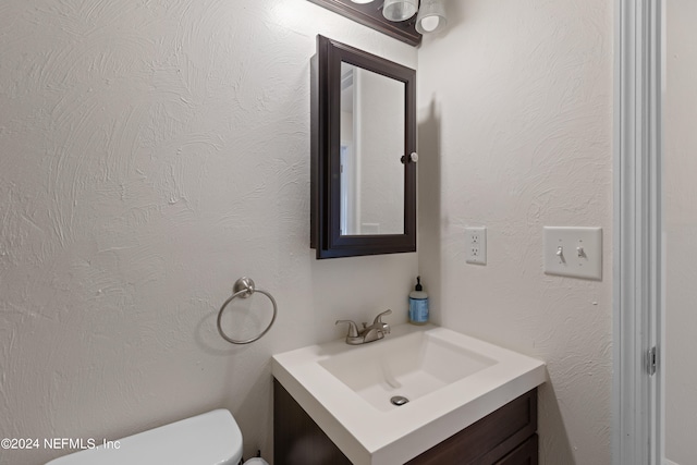 half bathroom with vanity, toilet, and a textured wall