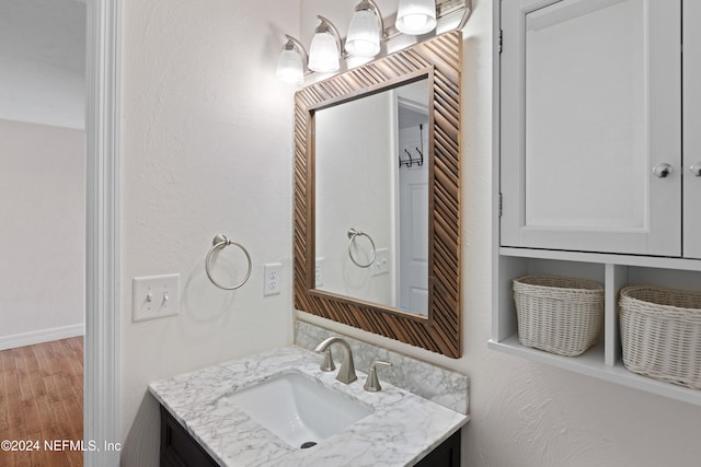 bathroom with baseboards, wood finished floors, vanity, and a textured wall