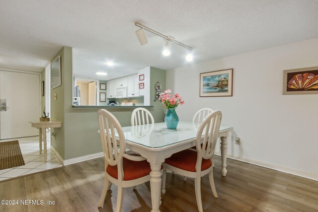 dining space with light hardwood / wood-style flooring, a textured ceiling, and rail lighting