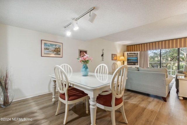 dining room featuring rail lighting, hardwood / wood-style flooring, and a textured ceiling