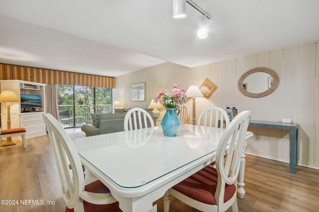 dining room with a textured ceiling, track lighting, wood-type flooring, and wooden walls