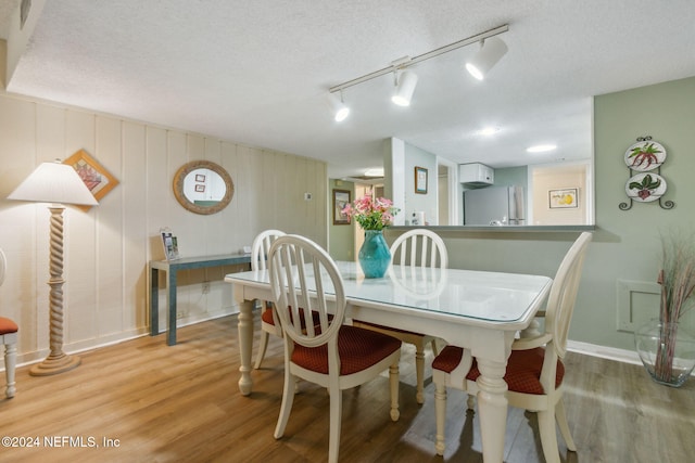 dining room featuring wood walls, a textured ceiling, track lighting, and light wood-type flooring