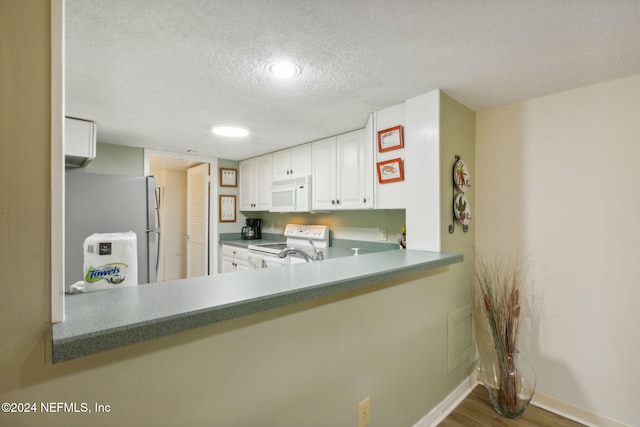 kitchen with kitchen peninsula, hardwood / wood-style floors, white cabinetry, a textured ceiling, and white appliances