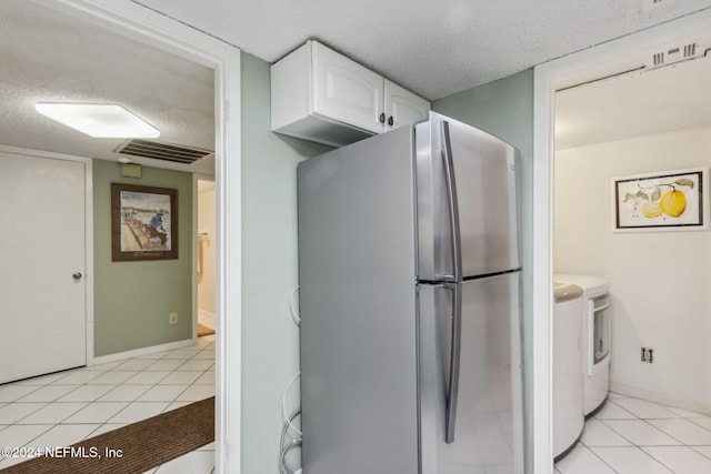 kitchen featuring washer and dryer, white cabinets, light tile patterned flooring, and stainless steel refrigerator