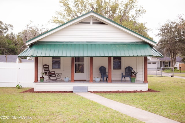 rear view of property featuring covered porch, fence, metal roof, and a yard