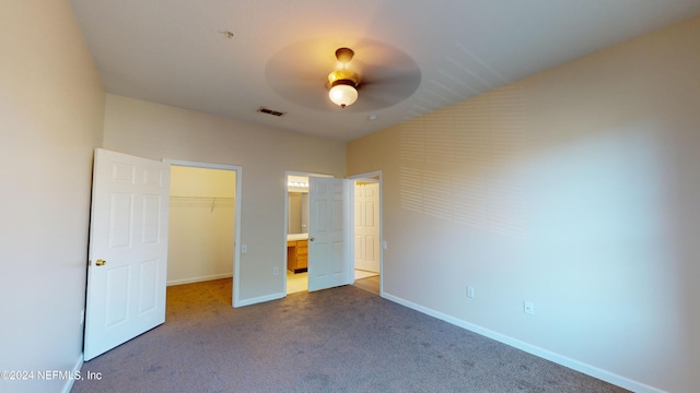 unfurnished bedroom with a spacious closet, carpet flooring, a closet, and ceiling fan