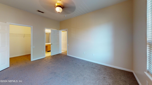 unfurnished bedroom featuring a spacious closet, carpet, a closet, and ceiling fan