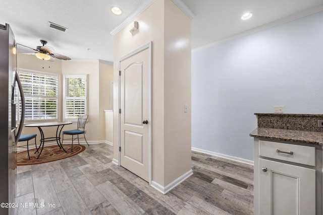 kitchen with dark stone countertops, ornamental molding, light wood-type flooring, white cabinetry, and stainless steel refrigerator