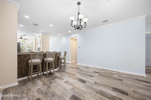 kitchen featuring light wood-type flooring, ceiling fan with notable chandelier, decorative light fixtures, ornamental molding, and a breakfast bar