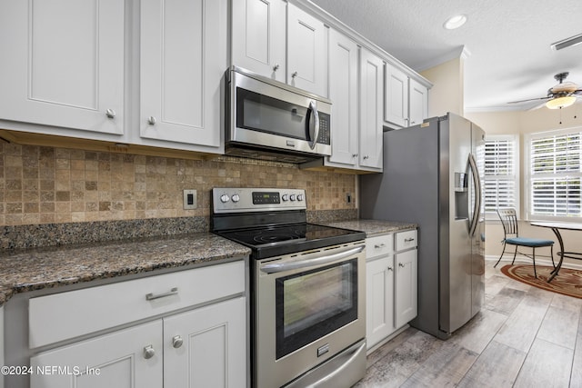 kitchen featuring white cabinetry, dark stone countertops, light hardwood / wood-style floors, crown molding, and stainless steel appliances