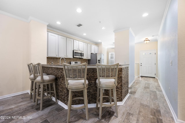 kitchen with appliances with stainless steel finishes, kitchen peninsula, a kitchen breakfast bar, and white cabinets