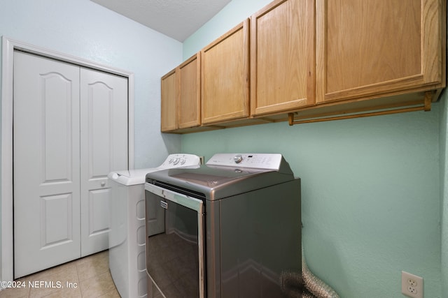 clothes washing area featuring light tile patterned floors, a textured ceiling, washing machine and dryer, and cabinets