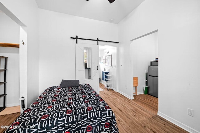 bedroom with hardwood / wood-style floors, a barn door, stainless steel refrigerator, and ceiling fan