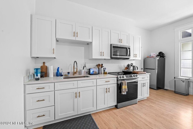 kitchen with sink, appliances with stainless steel finishes, light hardwood / wood-style floors, and white cabinets