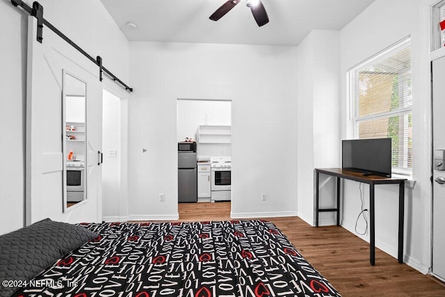 bedroom with ceiling fan, hardwood / wood-style flooring, a barn door, and stainless steel fridge