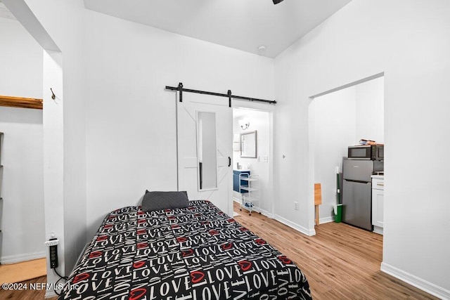 bedroom featuring a barn door, light hardwood / wood-style flooring, ensuite bathroom, and stainless steel refrigerator