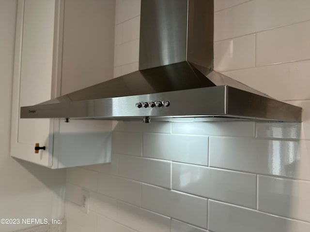 details with wall chimney exhaust hood, white cabinets, and tasteful backsplash