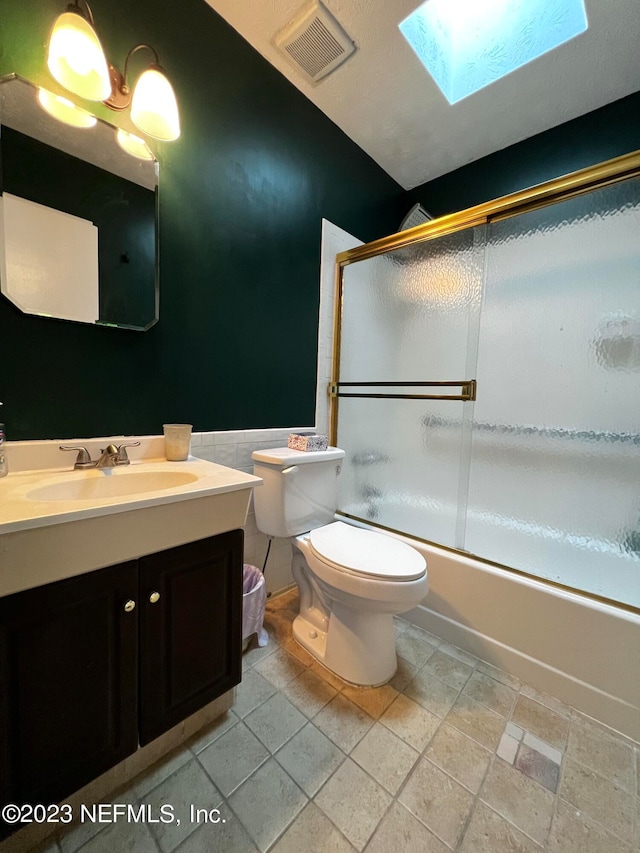 full bathroom featuring toilet, a skylight, vanity, and shower / bath combination with glass door