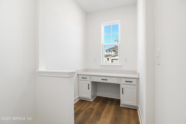 unfurnished office featuring dark hardwood / wood-style floors and built in desk