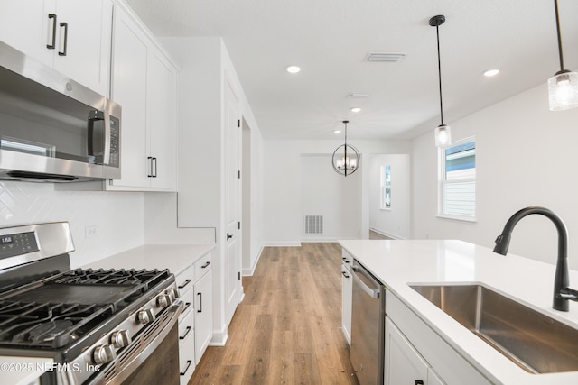 kitchen featuring sink, white cabinetry, stainless steel appliances, decorative light fixtures, and light wood-type flooring