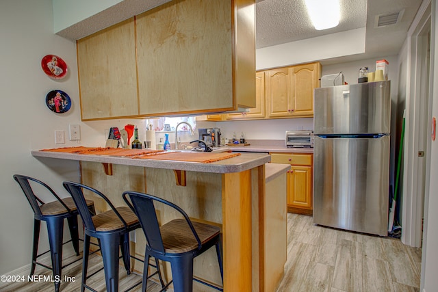 kitchen featuring a breakfast bar, stainless steel fridge, light wood-type flooring, and kitchen peninsula