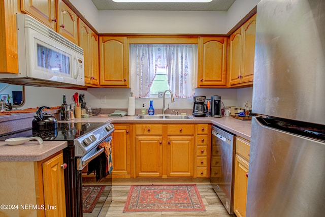 kitchen with sink, appliances with stainless steel finishes, a textured ceiling, and light hardwood / wood-style floors