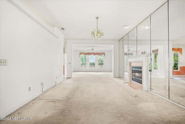 unfurnished living room with a textured ceiling, a tiled fireplace, light colored carpet, and ceiling fan with notable chandelier