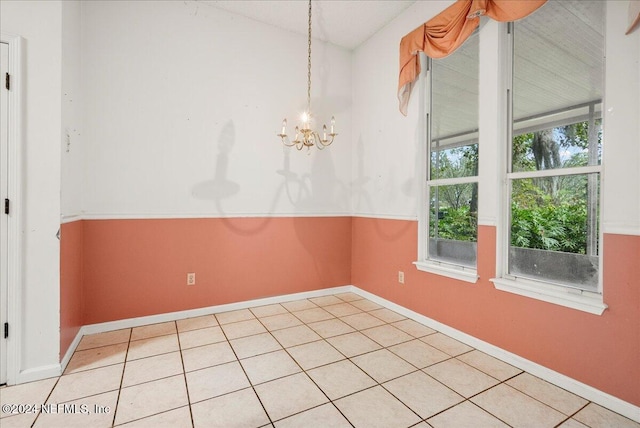 tiled spare room with a notable chandelier