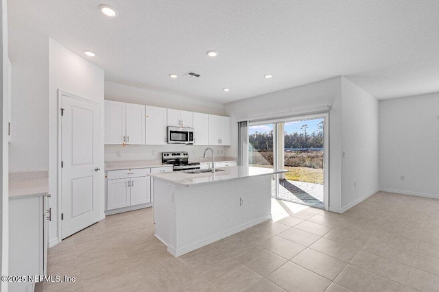 kitchen featuring sink, light tile patterned floors, an island with sink, stainless steel appliances, and white cabinets