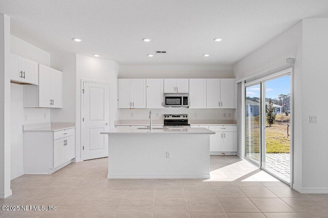 kitchen with appliances with stainless steel finishes, an island with sink, sink, white cabinets, and light tile patterned floors