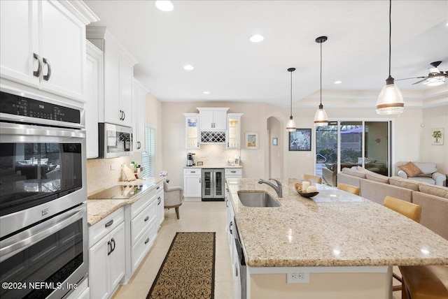 kitchen featuring sink, beverage cooler, backsplash, a center island with sink, and appliances with stainless steel finishes