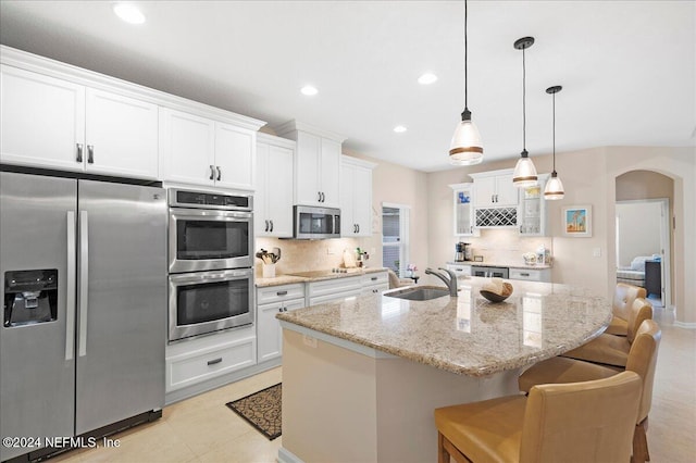 kitchen with a breakfast bar, stainless steel appliances, sink, white cabinets, and an island with sink