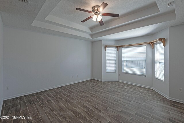 unfurnished room featuring ceiling fan, a raised ceiling, and a textured ceiling