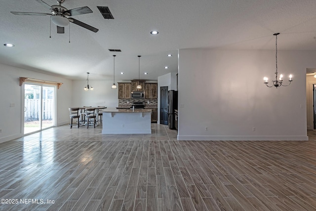 unfurnished living room with ceiling fan with notable chandelier, a textured ceiling, and light hardwood / wood-style floors