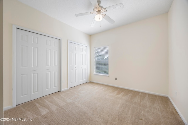 unfurnished bedroom featuring multiple closets, light colored carpet, and ceiling fan