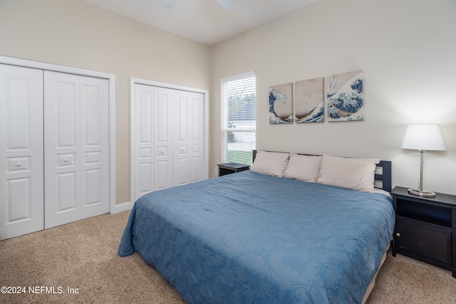 bedroom with ceiling fan, light colored carpet, and multiple closets