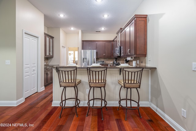 kitchen with stainless steel appliances, a peninsula, decorative backsplash, dark countertops, and dark wood finished floors