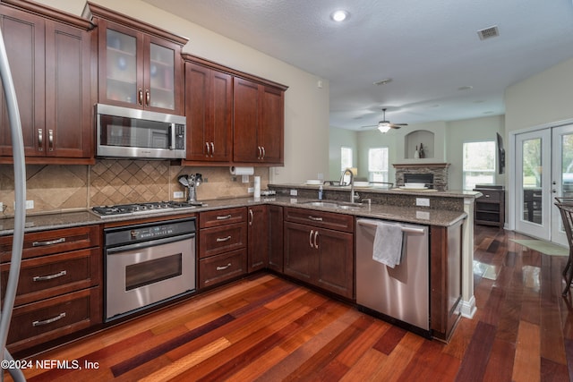 kitchen featuring stainless steel appliances, visible vents, glass insert cabinets, a sink, and dark stone countertops