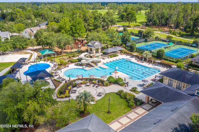 pool featuring a patio, a water slide, and a view of trees