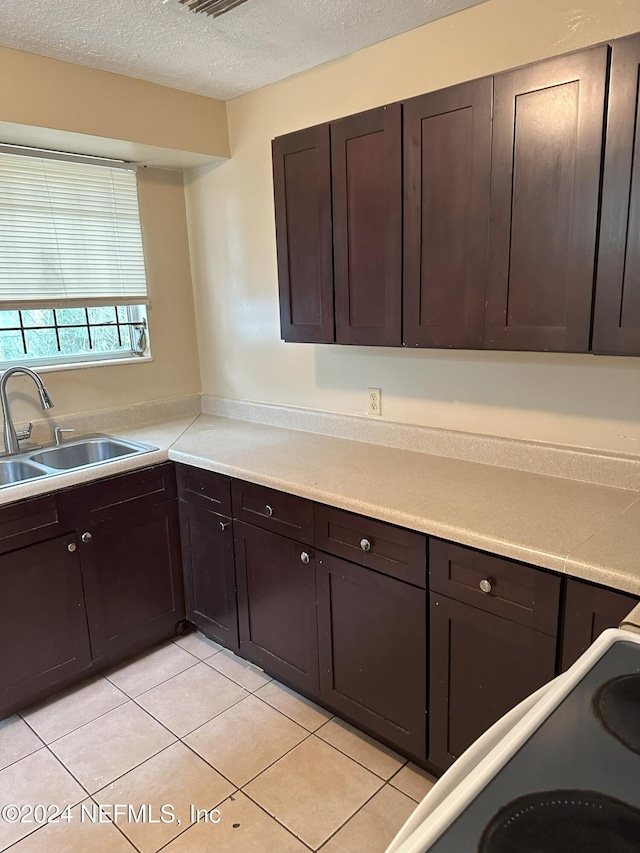 kitchen featuring sink, range, a textured ceiling, dark brown cabinets, and light tile patterned floors