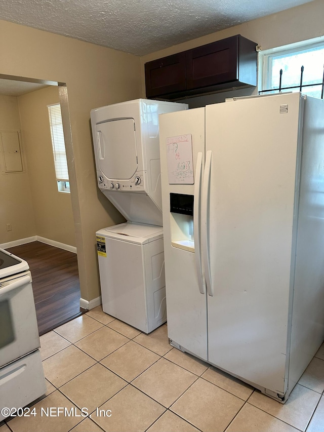 laundry area featuring stacked washer / drying machine, a textured ceiling, and light tile patterned floors