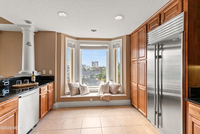 kitchen featuring light tile patterned floors, appliances with stainless steel finishes, a textured ceiling, decorative columns, and dark stone countertops